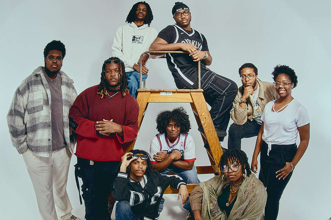 a group of men and women gather around a wooden step ladder and stand for a photo at different heights.